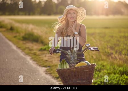 Porträt einer schönen Frau lächelnd glücklich, während sie ein gestreiftes Hemd trägt und ein Fahrrad in der Landschaft an einem sonnigen Tag fährt Stockfoto