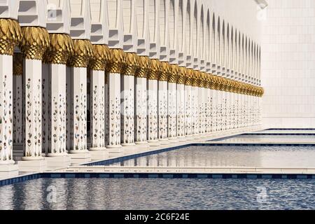 Blick auf die weißen Säulen der Abu Dhabi Moschee, die sich an einem sonnigen Tag im Wasser des Pools spiegeln. Stockfoto