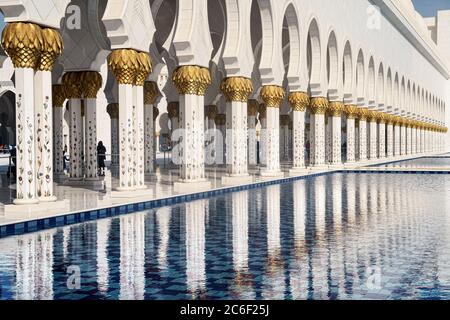 Blick auf die weißen Säulen der Abu Dhabi Moschee, die sich an einem sonnigen Tag im Wasser des Pools spiegeln. Stockfoto