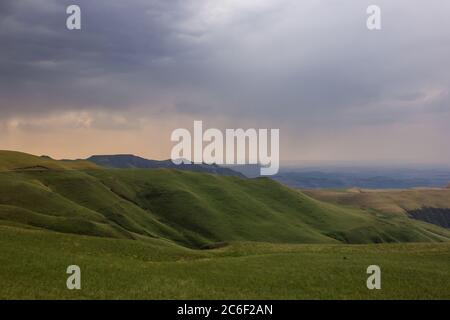 Von dem Gras bedeckt schräg der Drakensberg Berge, Südafrika, mit Regen in der Ferne Stockfoto