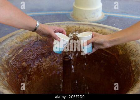 Schöpfen Sie Mineralwasser aus dem Brunnen in die Tassen im Spa Stockfoto