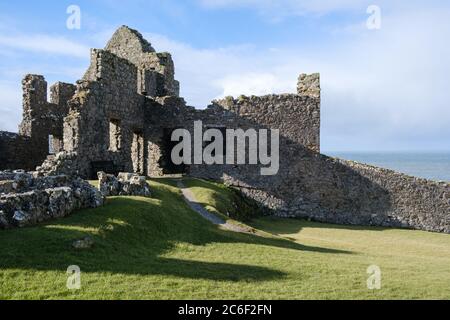 Dunluce Castle ruiniert vor einem wunderschönen hellblauen Himmel, inmitten üppig grünen Grases, in der Nähe von Portrush in Co. Antrim, Nordirland. Stockfoto