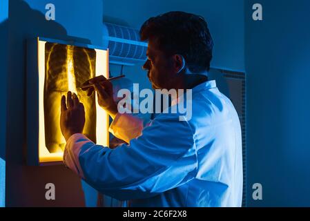 Ein Arzt in einer weißen Robe untersucht eine Röntgenaufnahme der Lunge oder Brust in Neonlicht. Ein Konzept zum Thema Medizin. Stockfoto