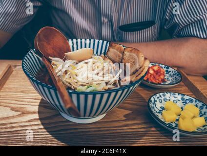 Der Mann wird seine frisch zubereiteten Ramen in einem koreanischen Café mit Kimchee und Daikon-Rettich als Beilagen essen Stockfoto