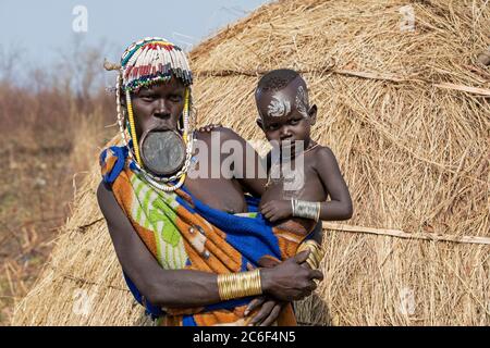 Schwarze Frau mit Kind des Mursi Stammes trägt Lippenplatte und Perlen im Mago Nationalpark in der Nähe von Jinka, Debub Omo Zone, Süd-Äthiopien, Afrika Stockfoto