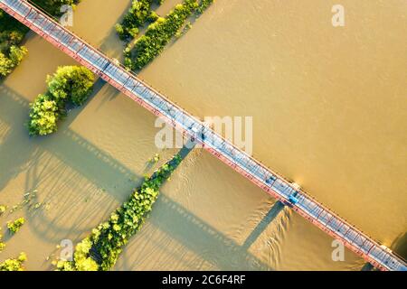 Luftaufnahme einer schmalen Straßenbrücke, die sich über einen schlammigen, breiten Fluss in grüner ländlicher Umgebung erstreckt. Stockfoto