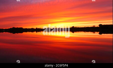 Symmetrie des Himmels in einem See bei Sonnenaufgang. Wolken, die sich auf dem Wasser spiegeln. Ferienlandschaft am Meer. Ruhige entspannende Szene mit einem schönen bunten Stockfoto