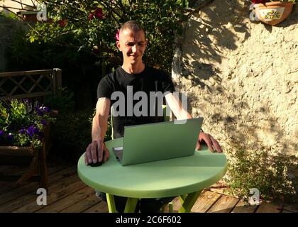 Mann, der zu Hause in seinem Garten an einem Laptop arbeitet. Arbeit für soziale Distanzierung. Online-Shopping mit dem Internet. Telearbeitkonzept. Stockfoto