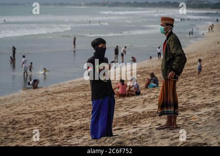 Badung, Bali, Indonesien. Juli 2020. Menschenherden in Kuta Beach warten auf Sonnenuntergang. Die lokale Regierung beginnt, die berühmte touristische Ikone des Kuta Beach für die Einwohner von Bali als eine Phase des "neuen normalen" Plans wieder zu öffnen. Kuta Beach ist seit dem 30. März 2020 wegen Covid-19 Coronavirus-Bedenken geschlossen. Kredit: Dicky Bisinglasi/ZUMA Wire/Alamy Live Nachrichten Stockfoto