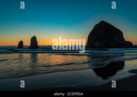 Der orange Sonnenuntergang zeigt die Silhouette des Haystack Rock und die Vögel am Cannon Beach in Oregon Stockfoto