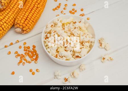 Popcorn in einer Schüssel auf weißem Holzhintergrund mit Ähren aus Mais Stockfoto