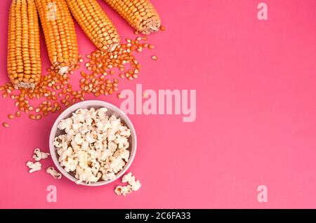 Popcorn in einer Schüssel auf rosa Hintergrund mit Kopie Platz mit Maiskolben Stockfoto