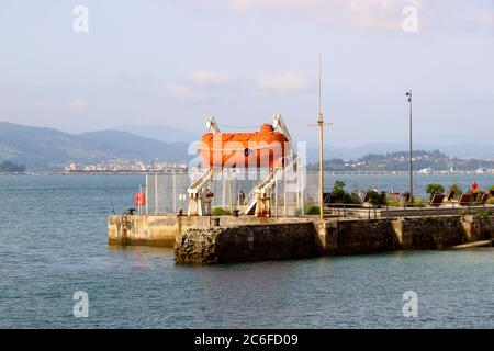 Leuchtend orange stillgelegte Kapsel Leben Boot in einem weißen Startrahmen neben der Bucht in Santander Cantabria Spanien aufgehängt Stockfoto