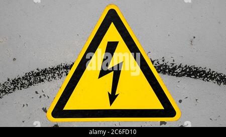Schmutziges gelbes Hochspannungswarnschild auf grauem Hintergrund isoliert Stockfoto