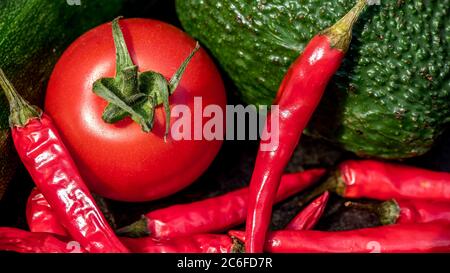 Draufsicht auf eine Vielfalt von frischen Lebensmitteln im Sonnenlicht, Tomaten, Chili, Avocado und Zucchini mit komplementären Farben Stockfoto