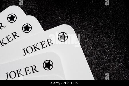 Vier weiße Joker-Spielkarten mit einer Karte, die aus dem Deck in der linken unteren Ecke auf der schwarzen Gusseisenfläche gezogen wurde, mit Kopierraum auf der rechten Seite Stockfoto