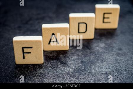 Stehende hölzerne Buchstabenfliesen bilden Wörter auf einer grauen Gusseisenoberfläche im Hintergrund, verblassen, Licht und Schatten Stockfoto