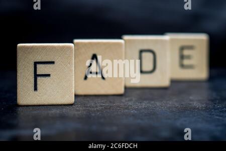 Stehende hölzerne Buchstabenfliesen bilden Wörter auf einer grauen Gusseisenoberfläche im Hintergrund, verblassen, nah oben Stockfoto