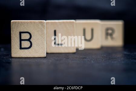 Stehende hölzerne Buchstabenfliesen bilden Wörter auf einer grauen Gusseisenoberfläche im Hintergrund, verschwimmen Stockfoto