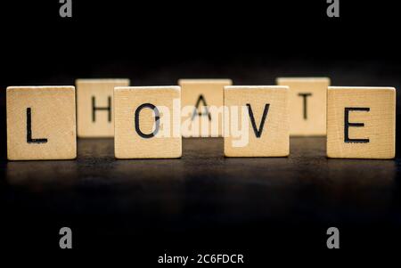 Stehende hölzerne Buchstabensteine bilden Wörter auf einer grauen Gusseisenoberfläche im Hintergrund, Liebe, Hass Stockfoto