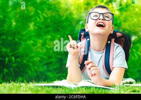 Überrascht Schulkind in Brille zeigt Finger nach oben neue Idee. Happy Kind Junge schreiben Hausaufgaben auf grünem Hintergrund. Online-Schulungen – E-Learning Stockfoto