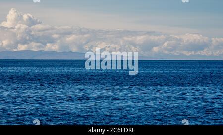 Glattes Wasser im Vordergrund in peru und schneebedeckte Gipfel der anden in bolivien, umhüllt von Frühlingswolken am Horizont im Hintergrund am See Stockfoto