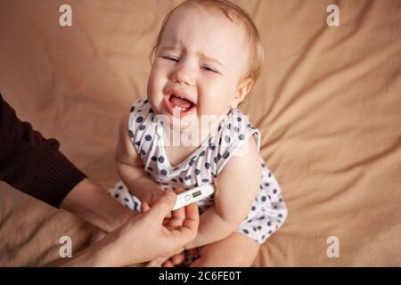 Frau, die die Temperatur ihrer kranken Tochter auf dem Bett überprüft Stockfoto