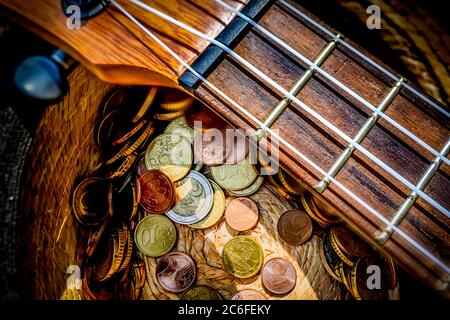 hut mit gespendeten Münzen und Ukulele-Musikinstrument auf der Oberseite, Geld verdienen mit Straßenmusik im Sonnenlicht Stockfoto