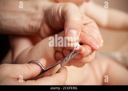 Ein Mann schneidet ihre Nägel Kinderhygiene. Männer Hände halten Nagelschere und ein Kind die Hand. Maniküre für Baby von Hand mit einer Schere, um den Nagel für cle schneiden Stockfoto