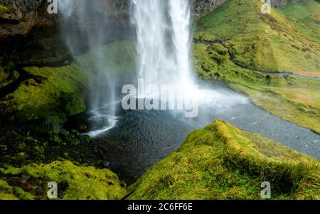 Blick auf den beliebten magischen Seljalandsfoss Wasserfall, der in einen kleinen Teich stürzt, umgeben von einem Fußweg durch grünes Gras, in der Nähe von Storidalur, island Stockfoto