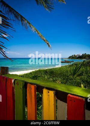 karibische Bucht mit Fischerbooten im Hintergrund und einem bunten Holzzaun im Vordergrund, aufrechtes Bild Stockfoto