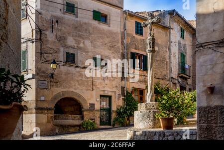 mediterraner Dorfplatz genannt carrer rei sanxo mit Kruzifix auf einem Pol von Sonnenlicht in dem kleinen Bergdorf valldemossa beleuchtet Stockfoto