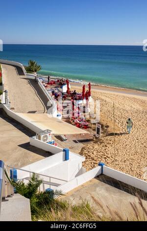 Touristen sitzen in der Wintersonne in der Snack Bar Carlota am Strand in Armacao de Pera an der Algarve Portugal Stockfoto