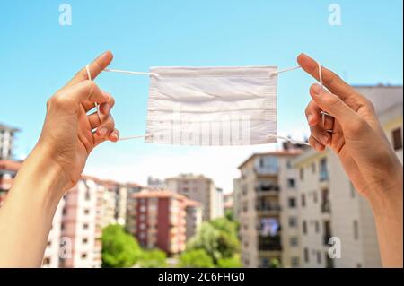 Frau hält eine Einweg-Gesichtsmaske gegen den blauen Himmel. Konzeptfoto. In der Normalisierungsphase werden Gesichtsmasken weiterhin verwendet. Stockfoto