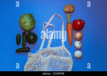 Umweltfreundlicher Baumwoll-Shopper und wiederverwendbarer Mesh-Einkaufstasche mit Gemüse auf blauem Hintergrund. Selektiver Fokus. Stockfoto