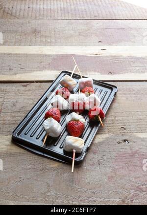 Gourmet gegrillte Erdbeere und Marshmallow auf Stick auf Holzspieße auf rustikalem Holzhintergrund. Stockfoto