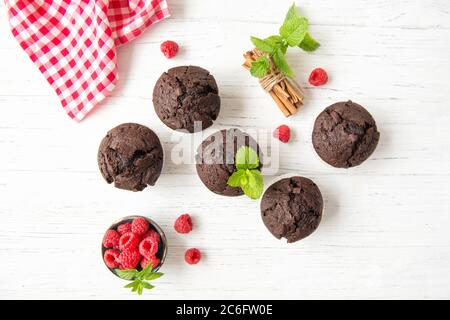 Schokoladenmuffins mit Himbeeren und Minzblättern auf weißem Holzhintergrund, Draufsicht Stockfoto