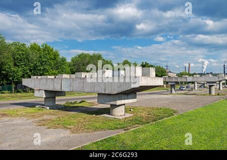 Stahlbetonstützen eines unfertigen Automobil-Viadukts vor dem Hintergrund von Rauchrohren im Industriegebiet der Stadt Stockfoto