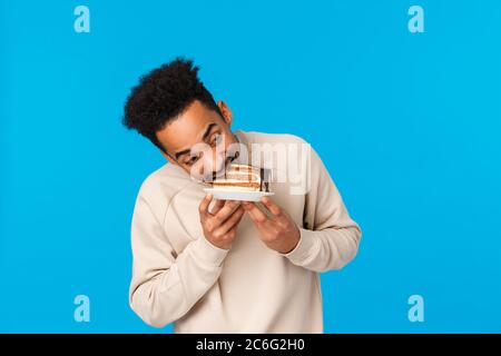 Guy stahlen Stückkuchen und aßen es schnell. Lustiger und süßer afrikanisch-amerikanischer Mann, der Teller hält, beißt köstliche Desserts, die Geburtstag feiern, genießen Stockfoto