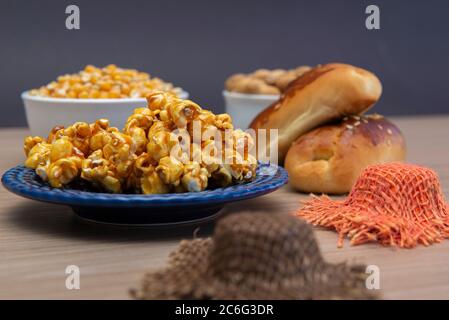 Nahaufnahme der typischen Juni Party Lebensmittel auf einem Holztisch: Popcorn, Maiskuchen, Maiskörner, Erdnussschoten und kleine Country Hüte. Speicherplatz kopieren. Selektiv Stockfoto