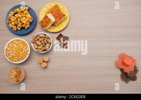 Draufsicht auf typische Juni-Party-Lebensmittel auf einem Holztisch: Popcorn, Maiskuchen, Maiskörner, Erdnussschoten, Erdnusskandeln (paçoca) und Dulce de leche Stockfoto