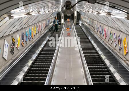 LONDON, ENGLAND - 8. JUNI 2020: London Underground Rolltreppe mit einem Mann in einer Gesichtsmaske, der während des COVID-19 soziale Distanzierungsmaßnahmen beobachtet Stockfoto