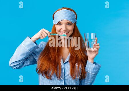 Enthusiastisch optimistisch, lebhaft Rothaarige Frau, Füchsin mit einem hübschen Lächeln, Zähneputzen mit Zahnbürste und Glaswasser, morgens aufwachen, immer Stockfoto