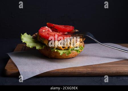 Die Hälfte der Wurger liegt auf dem Papier, die Gabel auf einem Brötchen, herzhaftes Rinderschnitzel, frisches Gemüse und viel Sauce Stockfoto