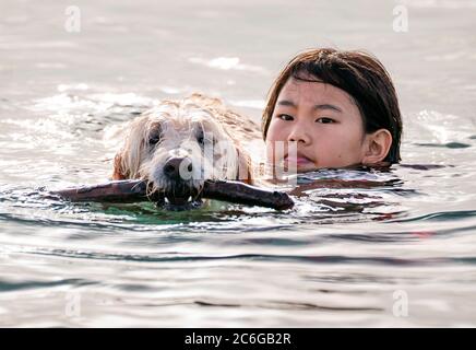 Juno Beach, Florida, USA. Juli 2020. Amelie Delarosa, hält die Familie Goldendoodle, Annie, flott, während sie im Meer spielen während eines frühen Morgenausflugs zum Hundestrand. Kredit: Greg Lovett/ZUMA Wire/Alamy Live Nachrichten Stockfoto