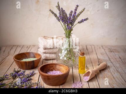 Flasche mit ätherischem Öl, Handtücher und Schalen mit Meersalz auf Holztisch. Lavendel Kosmetik, Spa und Wellness-Konzept. Stockfoto