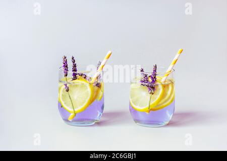 Gläser mit Lavendellimonade mit gelben Strohhalmen, grauer Hintergrund, Nahaufnahme. Stockfoto