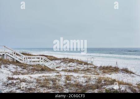 Weiß auf Weiß. Holztreppe über Küstendünen in Destin, Florida führt zu hellem weißen Sandstrand und hellgrünem Wasser des Golfs von Mexiko. Stockfoto