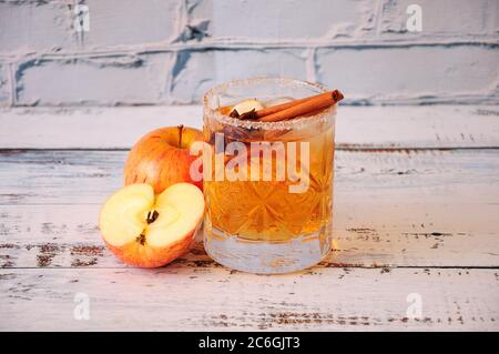 Ein tiefes Kristallglas aus Apfelwein mit Zimt und Anis steht auf einem Holztisch, neben einem halben und einem ganzen roten Apfel. Nahaufnahme. Stockfoto