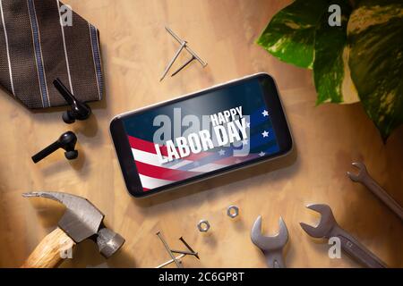 Happy Labor Day abstraktes Hintergrundkonzept. Flaches Lay Mockup Smartphone mit Happy Labor Day Text und wesentliche Arbeiter-Tools auf Geschäftsmann arbeiten Stockfoto